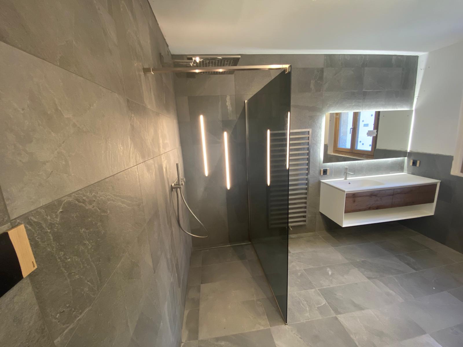Bagno arredato con doccia, mobile lavabo e specchio illuminato